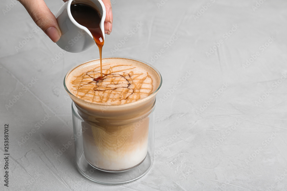 Canvas Prints Woman adding caramel syrup to latte macchiato on table, space for text