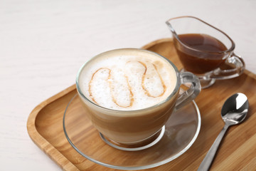 Tray with tasty caramel macchiato, spoon and syrup on table