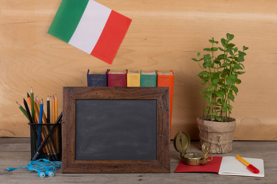 blank blackboard, flag of the Italy, books, chancellery on table and wooden background