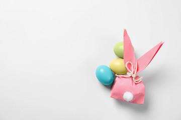 Easter bunny gift bag and dyed eggs on white background, top view