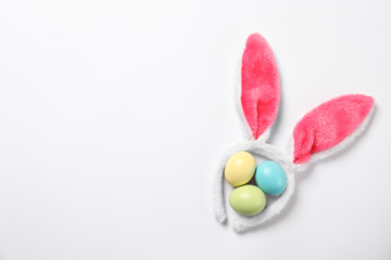 Funny headband with Easter bunny ears and dyed eggs white background, top view