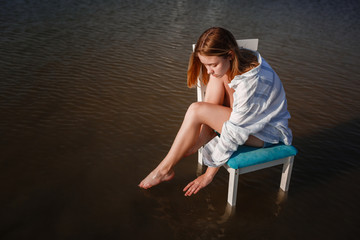 A beautiful teenage girl in a chair in the middle of a pond.