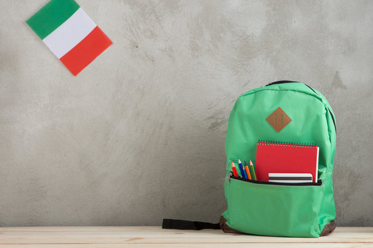 green backpack, flag of the Italy and notebooks against a cement wall