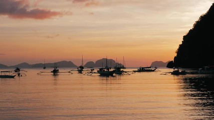 Traditional philippine boat bangka at sunset time. Beautiful sunset with silhouettes of philippine boats in El Nido, Palawan island, Philippines. Orange sky sunset paradise beach.