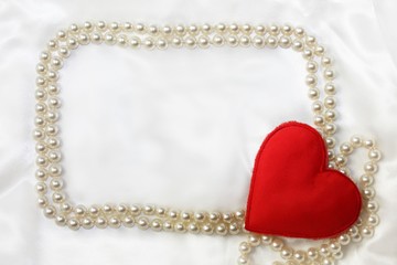 Silk white textile material background with glossy beads frame and textile heart decor in corner