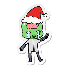 sticker cartoon of a big brain alien crying and giving peace sign wearing santa hat
