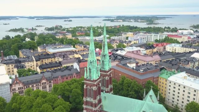 Aerial, orbit, drone shot around St Johns Church, overlooking the sea and buildings in the capital cityscape, on a cloudy, summer day, in Ullanlinna, Helsinki, Finland