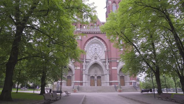 Static shot of the main entrance, to St Johns Church, filmed under green leaves and branches, on a cloudy, summer day, in Ullanlinna, Helsinki, Finland