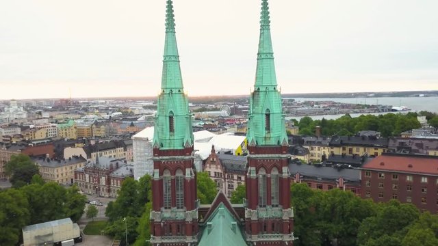 Aerial, drone shot flying between the two towers, on St Johns Church, overlooking the cityscape, on a cloudy, summer day, in Ullanlinna, Helsinki, Finland