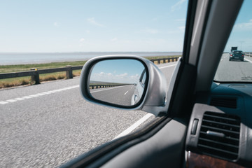 Fototapeta premium Side mirror reflecting the road and the the sky shot from the front seat while driving