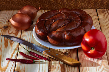 Preparation of a festive table, on a table of smoked sausage, a tomato, onions and acute red pepper to improve apetit.