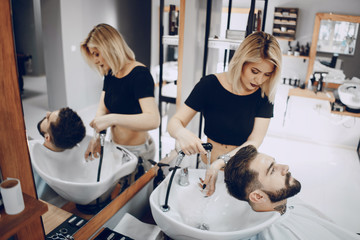 handsome young bearded guy sitting in an armchair in a beauty salon and the girl near  him washes...