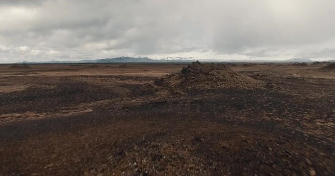 Vast volcanic plane aerial fly over with dimmu borgir rocks in front of snowy mountains, dramatic clouds in Iceland