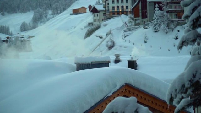 A smoking chimney on the snow-covered rooftop in the village of Samnaun, Switzerland. Slow motion, 120fps.