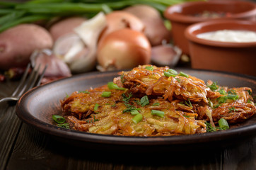 Fresh homemade tasty potato pancakes in clay dish with vegetables on wooden table