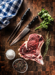 Rib eye steak with bone on butcher board with herbs salt pepper fork and knife
