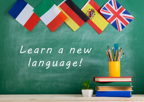 flags of Spain, France, Great Britain and other countries, blackboard with text "Learn a new language!", books and chancellery
