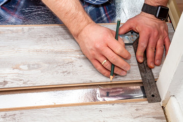 Man using measuring elbow and pencil while installing new wooden laminate flooring at home.