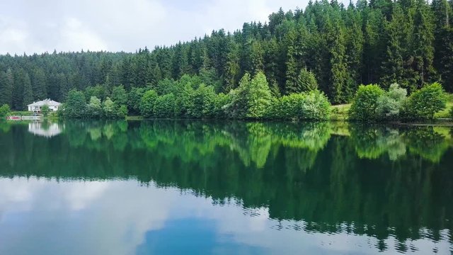 drone dolly sideways, close above the lake, a house in front of idyllic forest, lake reflecting pines anad clouds, in Karagol National Park, Savsat, Artvin, Turkey