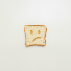 Slice of toast with a sad smile on a white background.
