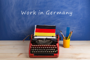 work abroad concept - red typewriter, flag of Germany on table and blackboard with text "Work in Germany"
