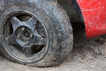 Fototapeta na wymiar black flat tire of a red car on a dirt road