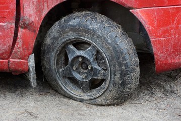 Fototapeta na wymiar one black flat tire of a red car on a dirt road
