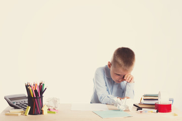 Cute little school boy with sad face sitting at his desk on white background.Unhappy intelligent children in shirt with blue eyes crying