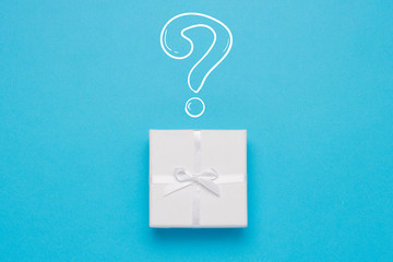 White gift box and Icon Question mark on a blue background. Minimalistic style. Concept surprise and suspense. Flat lay, top view