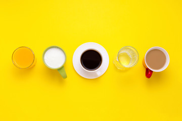 Obraz na płótnie Canvas Group of Drinks in Multicolored Cups, Black Coffee, Coffee with Milk, Yogurt, Just Water, Orange juice are put in one line on a Yellow background. Flat lay, top view