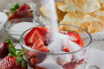 Close up of adding sugar to a bowl of sliced strawberries.  Motion blur of sugar being poured. ...