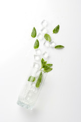 Spilled Glass with refreshing water, mint leaves and ice cubes on a light background