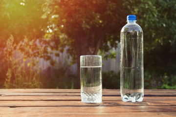 Glass of water and a plastic bottle with water on a wooden table in the spring garden