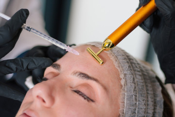 Aesthetic medicine treatment concept. Close up view of young woman getting cosmetic injection of botox in forehead.