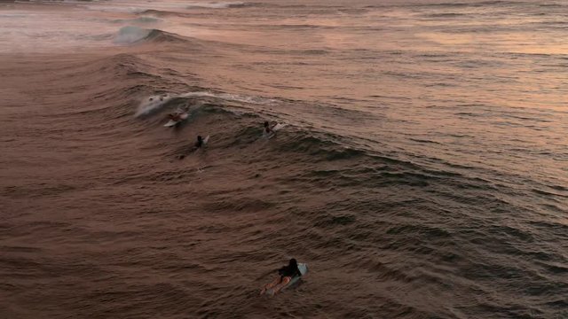 Aerial shot of surfers paddling out to catch the last wave before the sun sets.