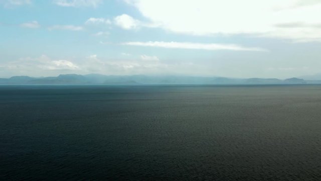 Moving drone shot above an open sea off the coast of Bali, Indonesia. Boats and mountains in the distance.