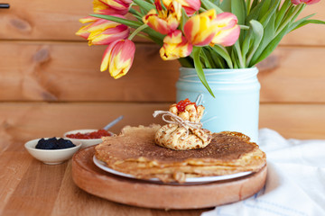 Fototapeta na wymiar Large round pancakes with red and black caviar. Envelopes from pancakes with filling. A bouquet of fresh spring tulbpans on the table and breakfast. Fotov rustic style. Copy space.