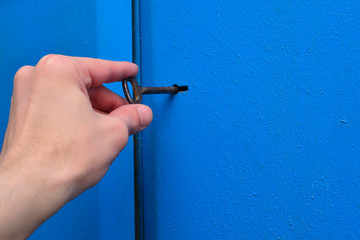 A hand is holding an old key in the keyhole. Blue, metal door with a textured surface. Concept:...