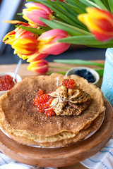 Large round pancakes with red and black caviar. Envelopes from pancakes with filling. A bouquet of fresh spring tulbpans on the table and breakfast. Fotov rustic style. Copy space.
