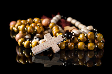 Wooden rosary beads with cross on black reflective background.