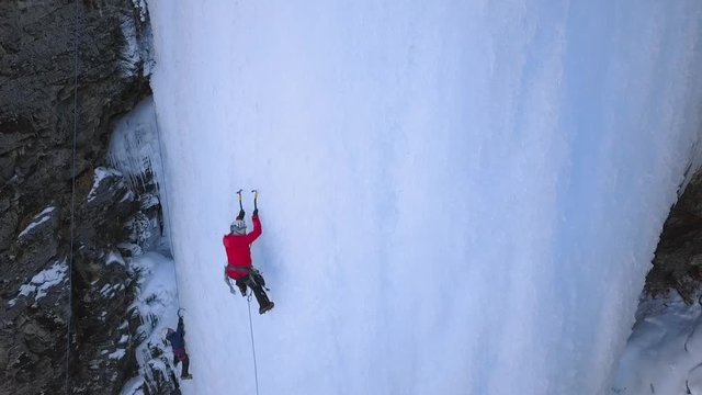 Alpinists use axe tools to climb to frozen waterfall. Aerial shot.