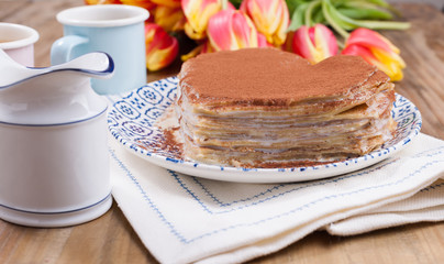 Two cups of aromatic coffee and pancakes with cream. Breakfast for two on a wooden background and a bouquet of red spring tulips. Free space for text.