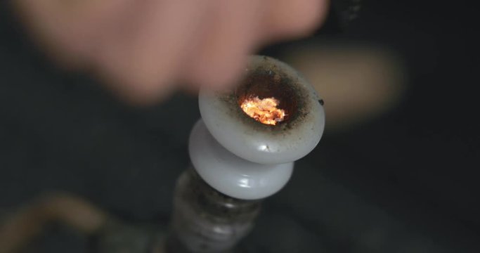 Cannabis turns to orange glowing embers as it's pulled through the stem of a bong and smoke is exhaled. Extreme close up.