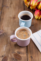Two cups of aromatic coffee and pancakes with cream. Breakfast for two on a wooden background and a bouquet of red spring tulips. Free space for text.