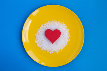 Red heart and salt in the yellow plate on the blue  background.Top view.Copy space.
