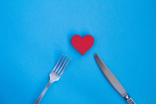 Red heart, knife and fork on the blue  background.Top view.Copy space.