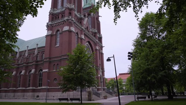 Static shot of St Johns Church, filmed under green trees, branches, full of leaves, hanging in the frame, on a overcast, summer day, in Ullanlinna, Helsinki, Finland
