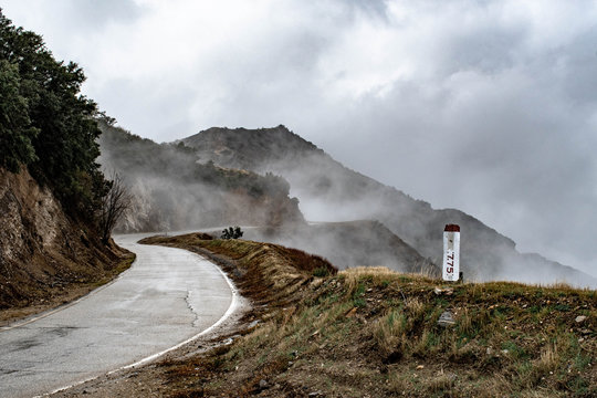 A wet and winding road running through mountains and fog 