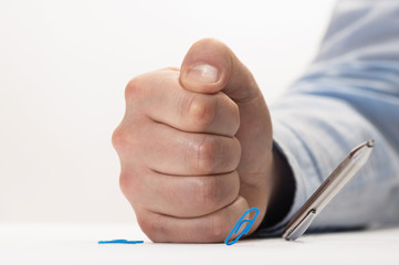 Angry man hits the table with his fist. Stationery items on the table bounce from his impact. Concept of anger.