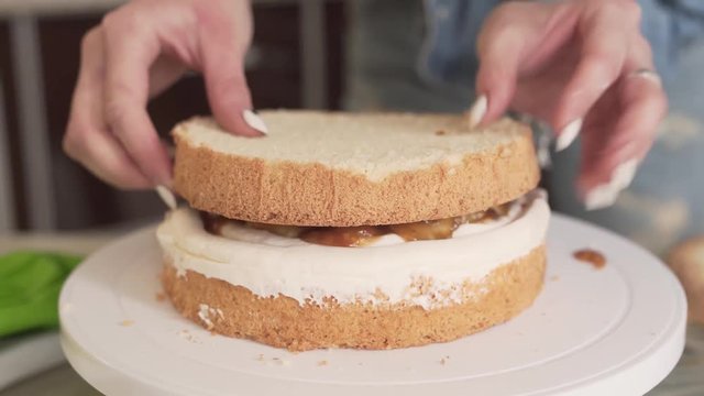 Close-up picture of a woman who is making a biscuit cake with a white cream and slices of caramelized pears.